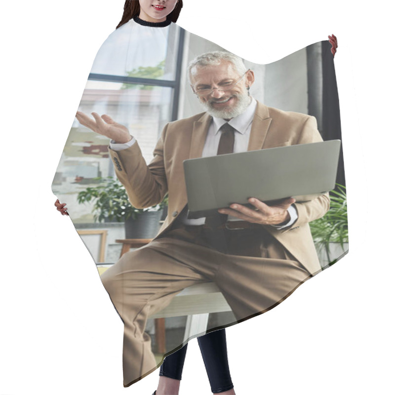 Personality  A Mature Man With A Beard Sits At A Desk, Holding A Laptop While Smiling And Gesturing With His Hand. Hair Cutting Cape