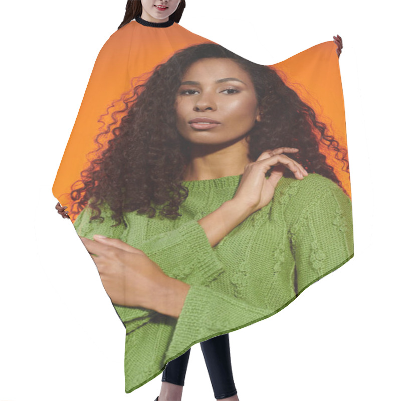 Personality  Curly Haired Woman In A Green Sweater Poses Against A Glowing Orange Background. Hair Cutting Cape