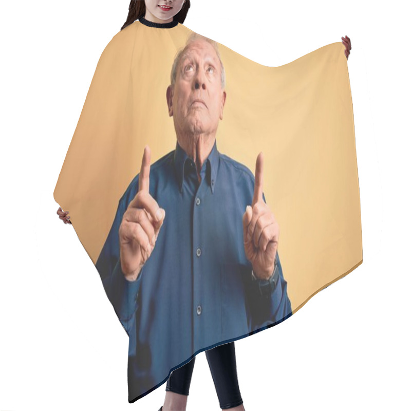 Personality  Grey Haired Senior Man Wearing Casual Blue Shirt Standing Over Yellow Background Pointing Up Looking Sad And Upset, Indicating Direction With Fingers, Unhappy And Depressed. Hair Cutting Cape