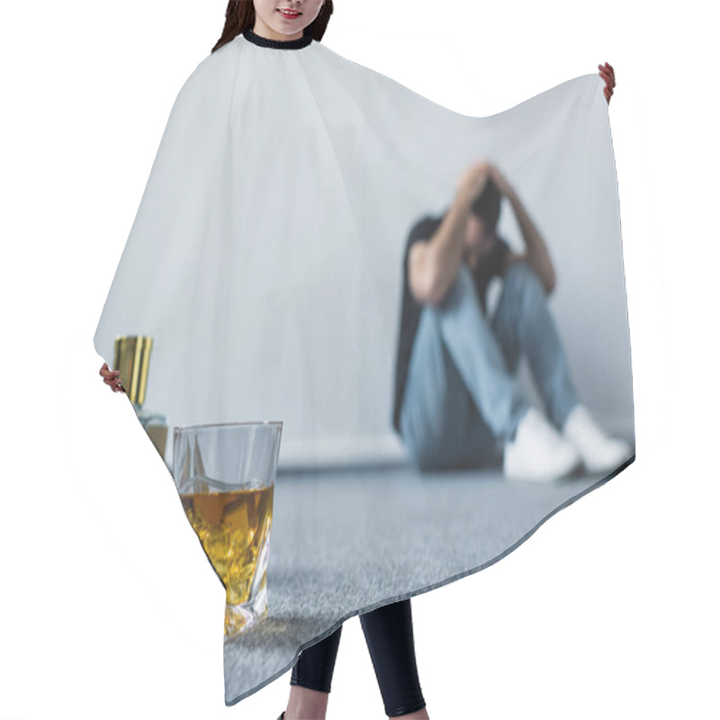 Personality  Selective Focus Of Suffering Man Sitting On Floor By White Wall Near Bottle And Glass With Whiskey Hair Cutting Cape