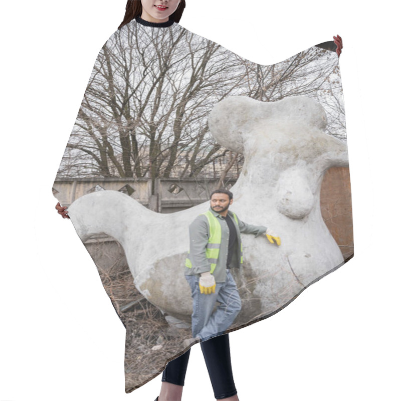 Personality  Indian Worker In Safety Vest And Gloves Looking Away While Standing Near Concrete Sculpture In Outdoor Waste Disposal Station, Garbage Sorting And Recycling Concept Hair Cutting Cape