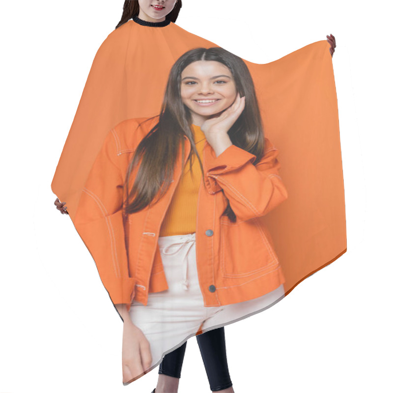 Personality  Portrait Of Joyful And Brunette Teenage Model In Denim Jacket And Pants Touching Face And Looking At Camera While Standing Isolated On Orange, Cool And Confident Teenage Girl Hair Cutting Cape