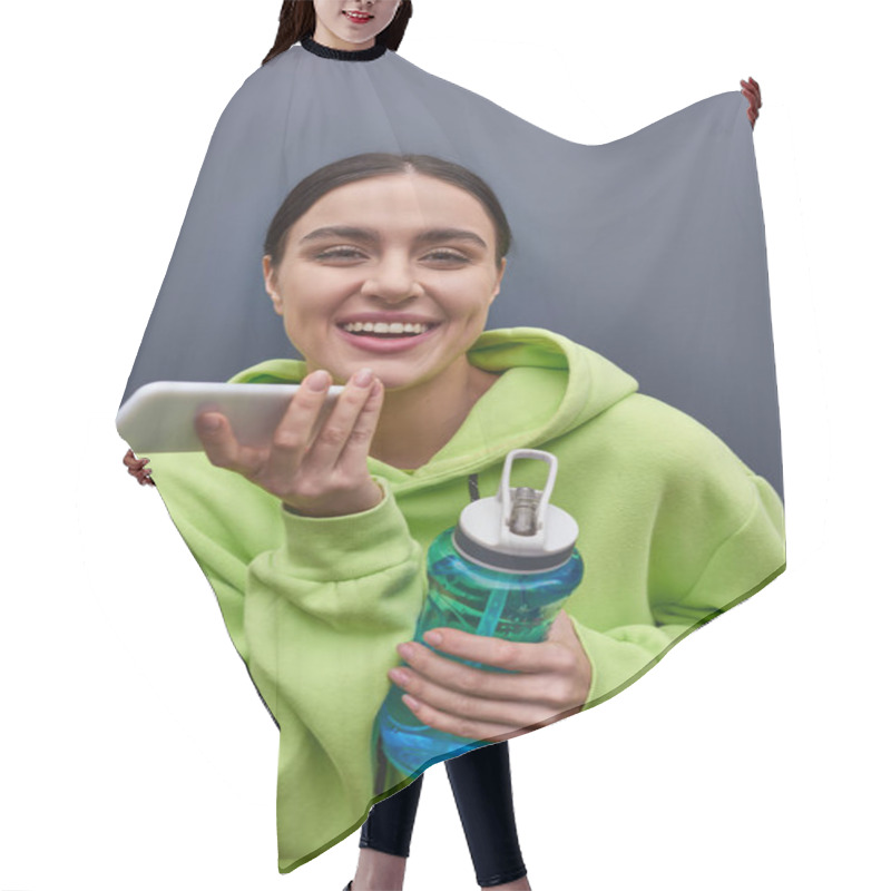 Personality  Cheerful Sportswoman In Hoodie Holding Bottle Of Water And Recording Audio Message On Smartphone Hair Cutting Cape