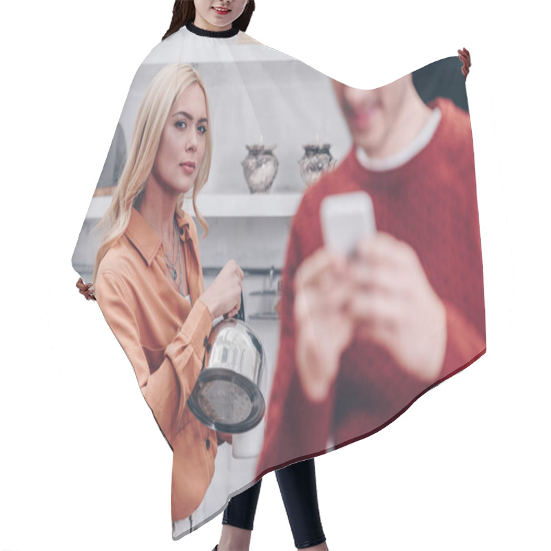 Personality  Selective Focus Of Jealous Young Woman With Kettle Looking At Husband Using Smartphone In Kitchen  Hair Cutting Cape