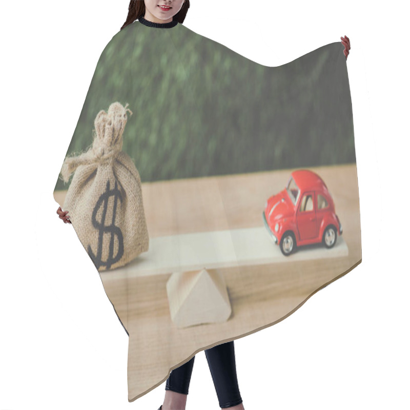 Personality  Red Miniature Car And Money Bag With Dollar Sign Balancing On Seesaw On Green Background Hair Cutting Cape