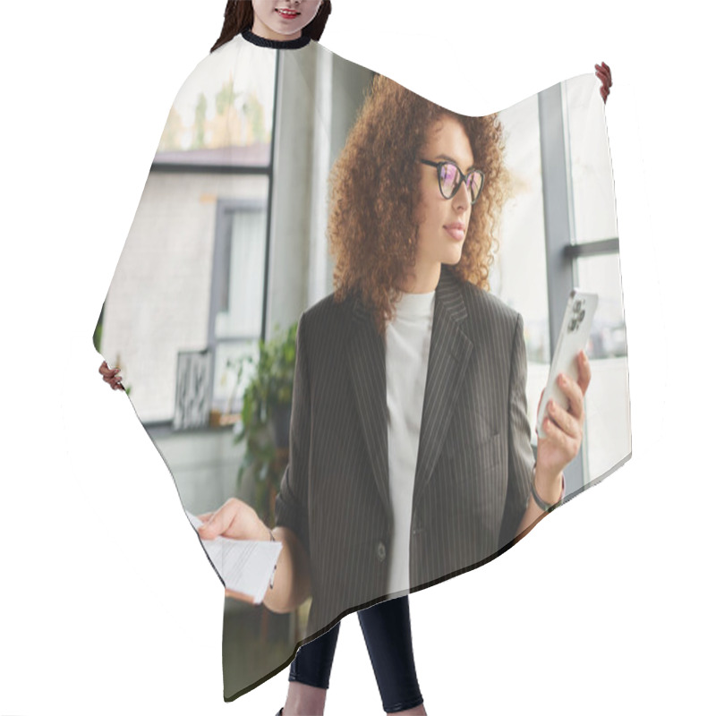 Personality  The Woman With Curly Hair Stands In A Stylish Office, Glancing At Her Phone And Holding Papers. Hair Cutting Cape