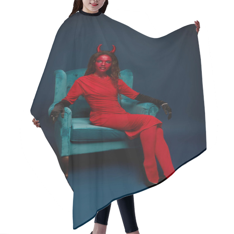 Personality  A Striking Woman Dressed As A Devil Lounges In A Teal Chair, Exuding Halloween Spirit. Hair Cutting Cape