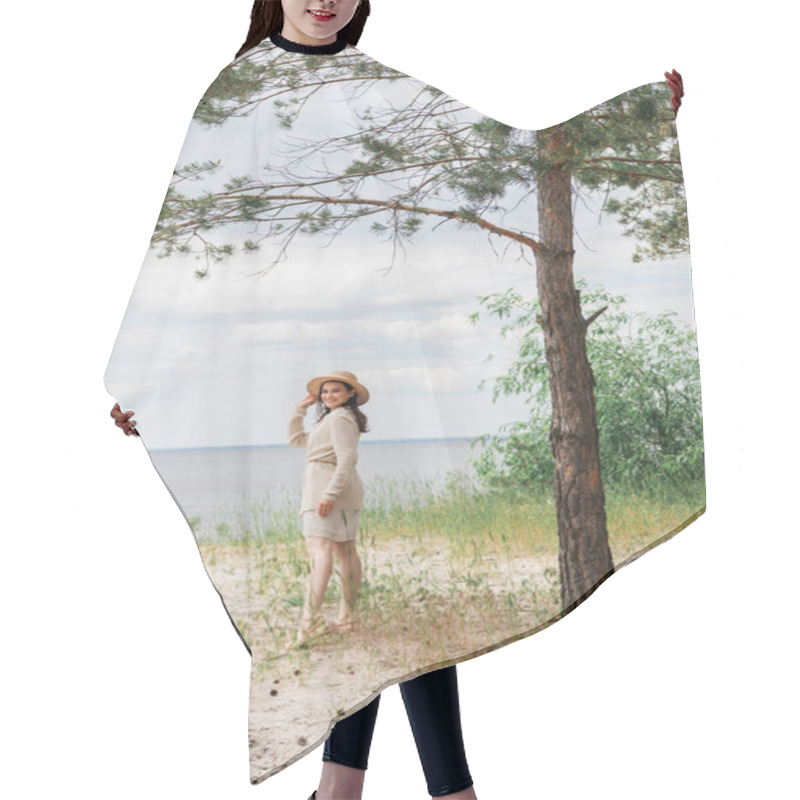 Personality  Full Length Of Smiling Young Woman Adjusting Straw Hat And Standing In Woods Near Lake Hair Cutting Cape