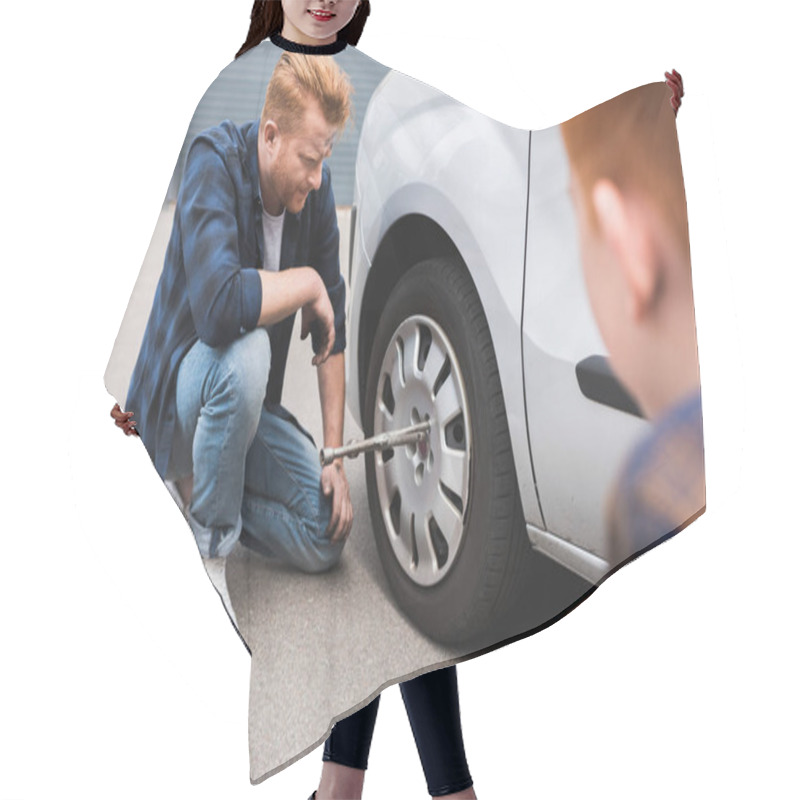 Personality  Father Changing Tire In Car With Wheel Wrench, Son Sitting Near Hair Cutting Cape