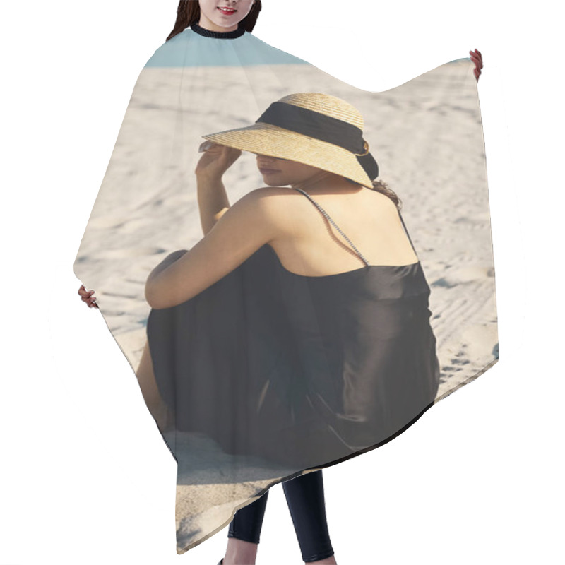 Personality  A Young Woman In A Black Sundress And Straw Hat Sits On The Sand, Her Gaze Lost In The Horizon. Hair Cutting Cape