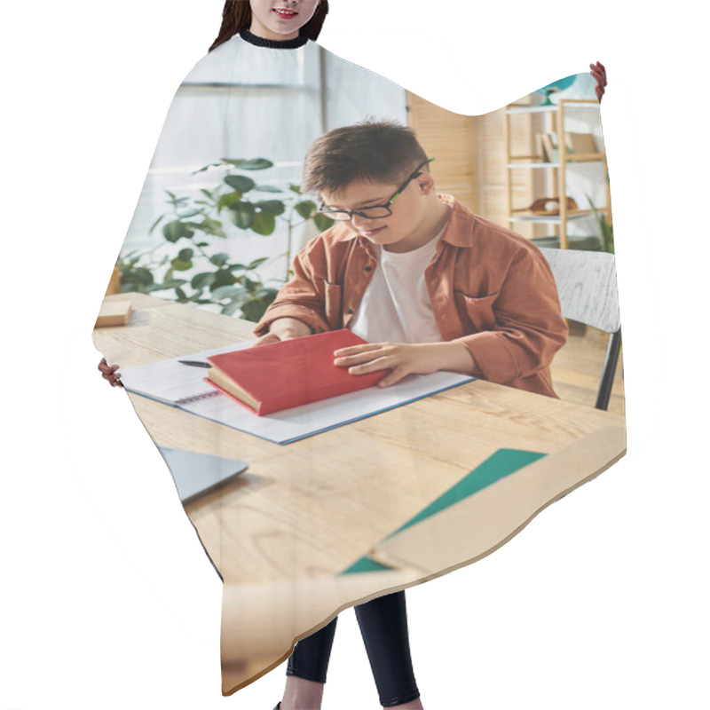 Personality  A Boy With Down Syndrome Sits At A Desk With A Laptop And A Book. Hair Cutting Cape