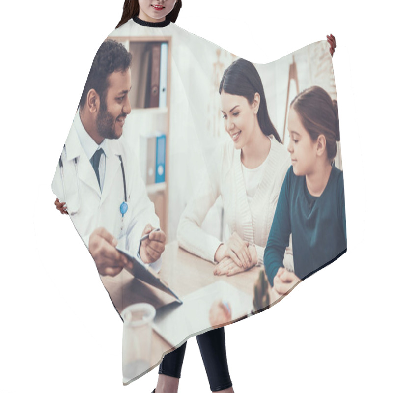 Personality  Indian Doctor Seeing Patients In Office. Doctor Is Showing Clipboard To Mother And Daughter. Hair Cutting Cape