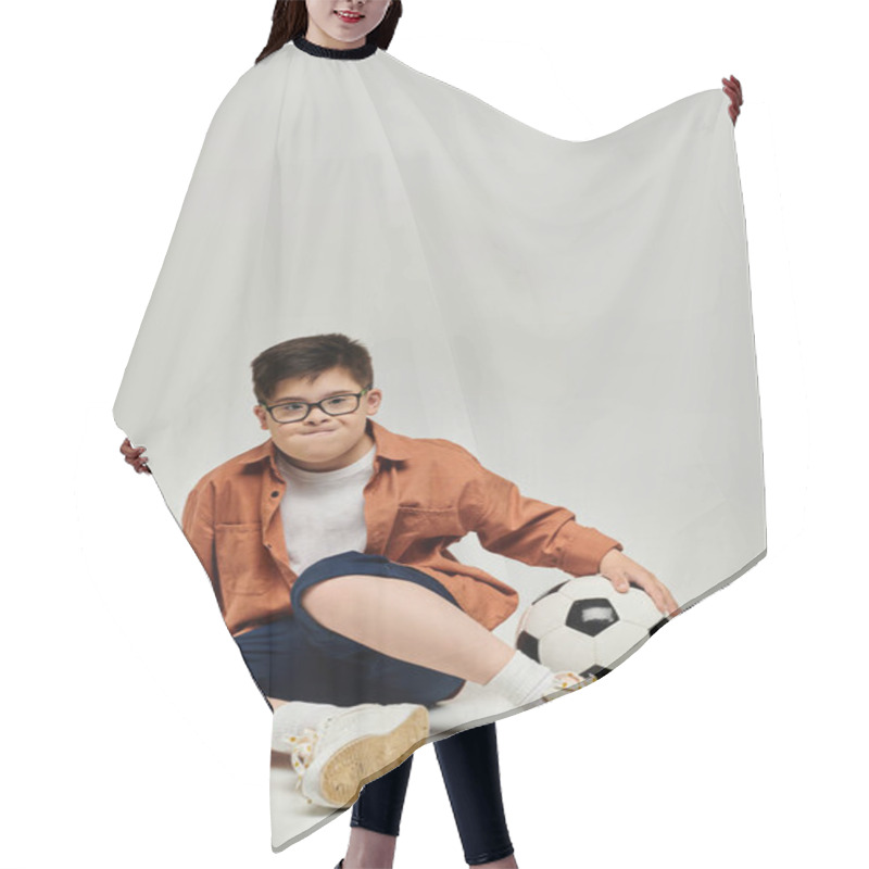 Personality  Little Boy With With Down Syndrome With Glasses Sits On Ground With Soccer Ball. Hair Cutting Cape