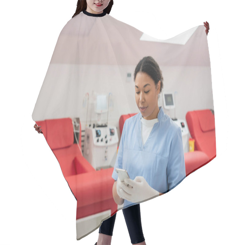 Personality  Multiracial Nurse In Blue Uniform And Latex Gloves Messaging On Mobile Phone Near Medical Chairs And Transfusion Machines In Blood Donation Center Hair Cutting Cape