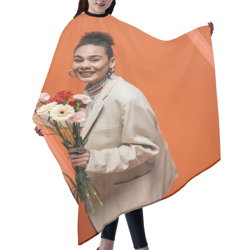 Personality  Cheerful Trendy Fashion Model In Chic Outfit With Sleek Bun Grasping Orange Framework And Flowers Hair Cutting Cape