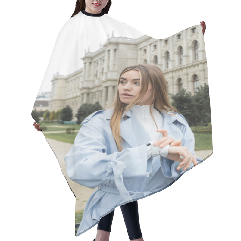 Personality  Young Woman In Blue Trench Coat Checking Time On Wristwatch While Waiting Near Historical Building In Vienna  Hair Cutting Cape