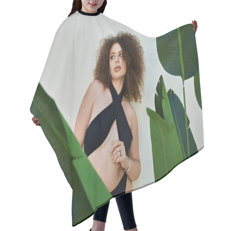 Personality  A Beautiful Woman With Curly Hair Poses In A Black Swimsuit Against A White Wall, Framed By Lush Green Foliage. Hair Cutting Cape