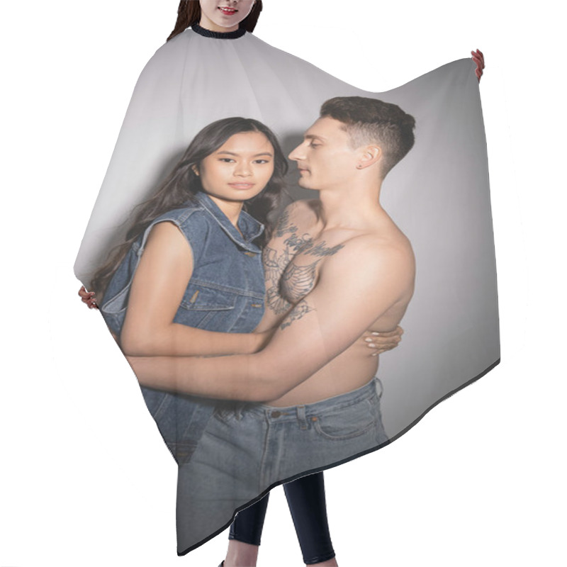 Personality  Brunette Asian Woman In Denim Vest Looking At Camera Near Muscular Tattooed Man On Grey Background Hair Cutting Cape