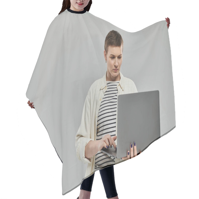 Personality  A Woman With Short Hair Stands In Front Of A Gray Background, Using A Laptop Computer. Hair Cutting Cape