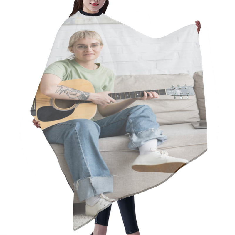 Personality  Young Woman In Glasses With Bangs And Tattoo Holding Acoustic Guitar And Learning How To Play Near Laptop And Sitting On Comfortable Couch, Looking At Camera In Modern Living Room At Home  Hair Cutting Cape