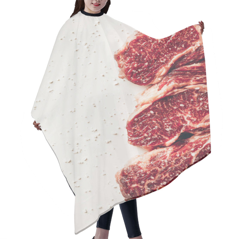 Personality  Elevated View Of Three Pieces Of Raw Meat Steaks And Scattered Salt On White Surface Hair Cutting Cape