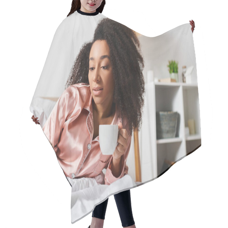 Personality  Curly African American Woman In Pajamas Enjoying Morning Coffee And Checking Her Cell Phone While Relaxing In Bed. Hair Cutting Cape