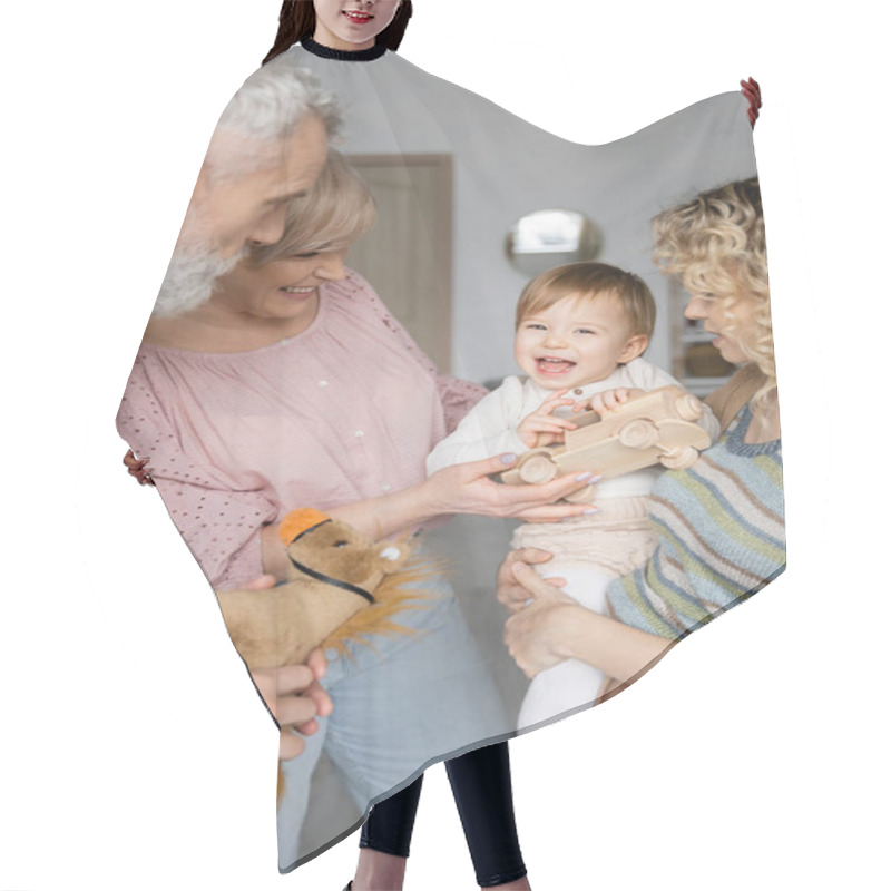 Personality  Baby Girl Holding Toy Car And Laughing Near Mom And Grandparents At Home Hair Cutting Cape