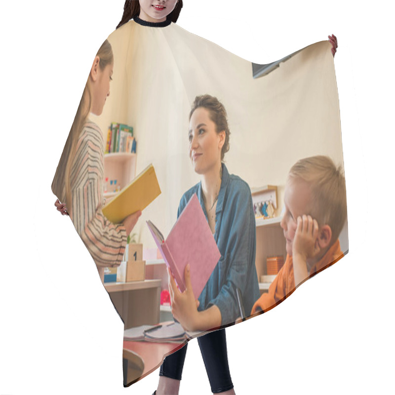 Personality  Girl With Book Standing Near Teacher And Boy Sitting At Desk In Classroom Hair Cutting Cape