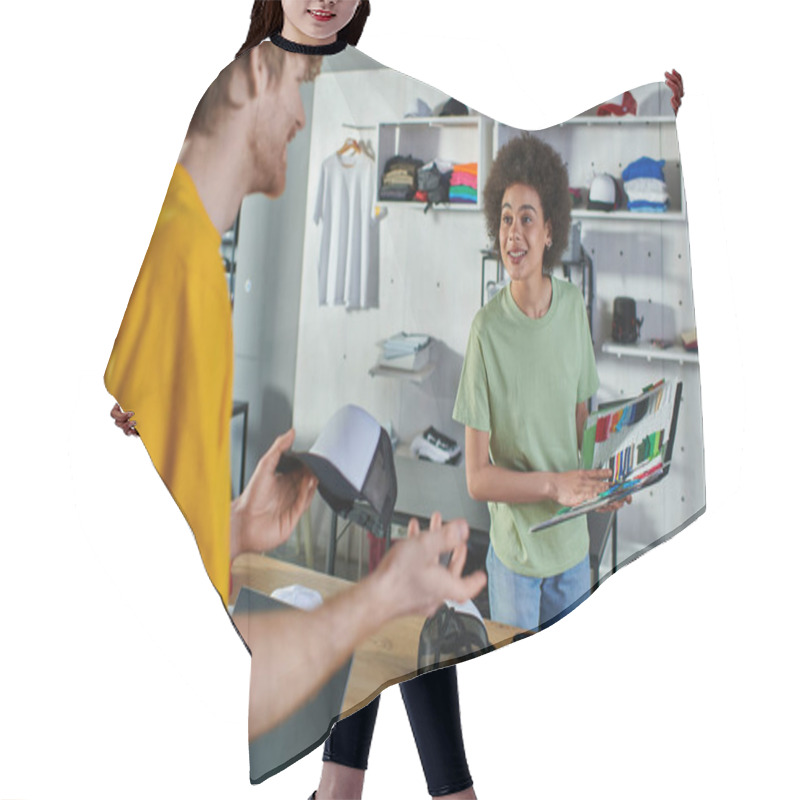 Personality  Smiling Young African American Designer Holding Cloth Samples Near Blurred Colleague With Snapback And Laptop With Blank Screen In Print Studio, Hands-on Entrepreneurship Concept  Hair Cutting Cape