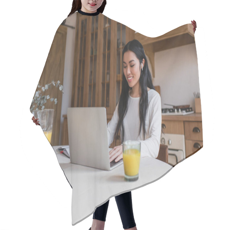 Personality  Smiling Young Asian Woman In Earphones Sitting On Table And Using Laptop In Kitchen Hair Cutting Cape