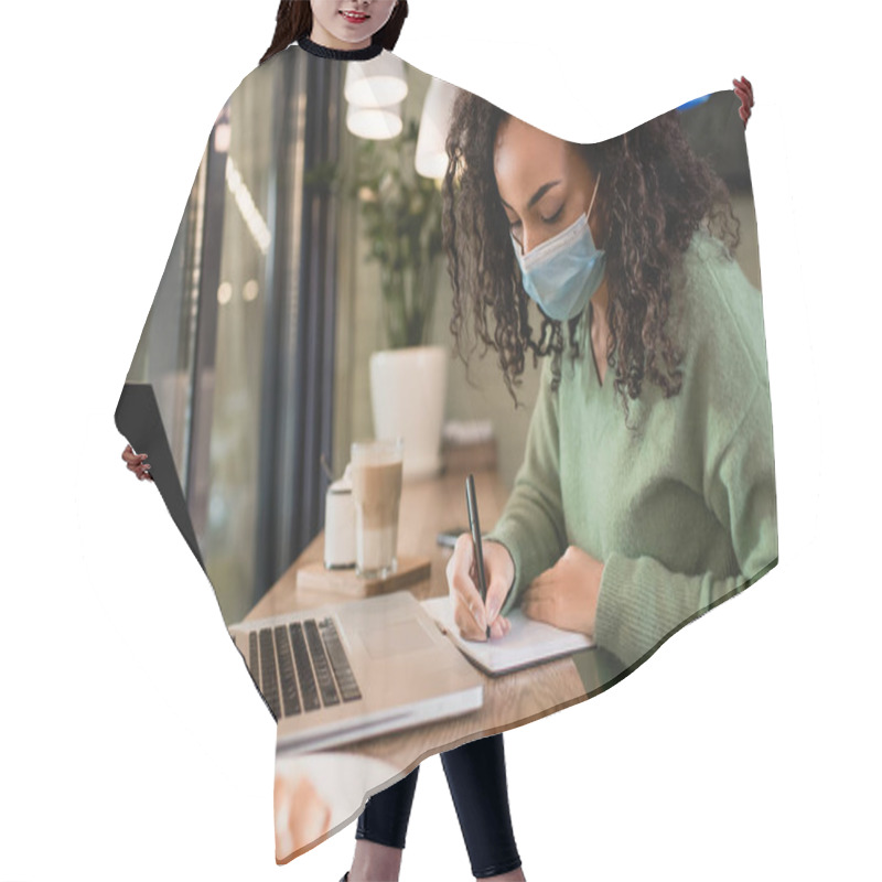 Personality  African American Woman In Medical Mask Writing In Notebook Near Laptop With Blank Screen On Table  Hair Cutting Cape