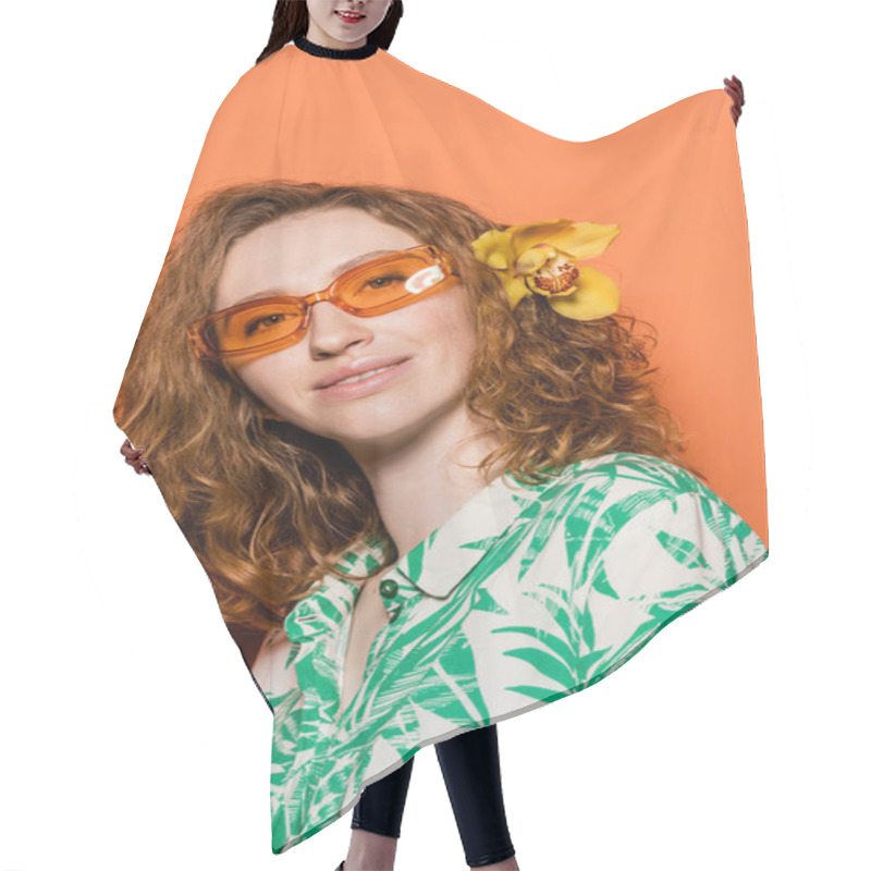 Personality  Positive Young Model With Orchid Flower In Red Hair, Natural Makeup And Sunglasses Posing In Blouse With Floral Print On Orange Background, Summer Casual And Fashion Concept, Youth Culture Hair Cutting Cape