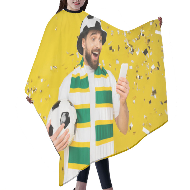 Personality  Amazed And Happy Sports Fan With Soccer Ball Watching Football Match On Smartphone Near Confetti On Yellow  Hair Cutting Cape