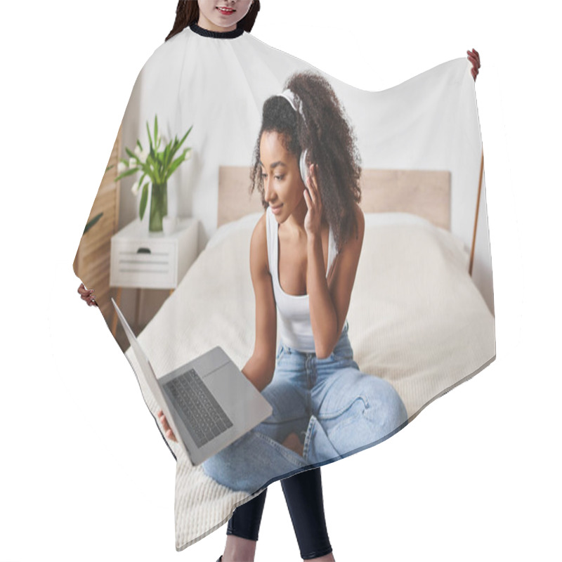 Personality  Curly African American Woman In Tank Top Sits On Bed Using Laptop Computer In Stylish Modern Bedroom. Hair Cutting Cape