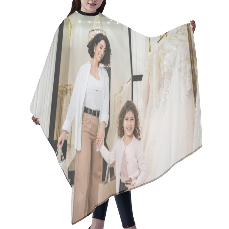 Personality  Happy Middle Eastern Bride With Brunette Hair In Beige Pants With White Shirt Holding Shopping Bags While Standing With Little Girl Near Wedding Dresses In Bridal Salon, Mother And Daughter  Hair Cutting Cape