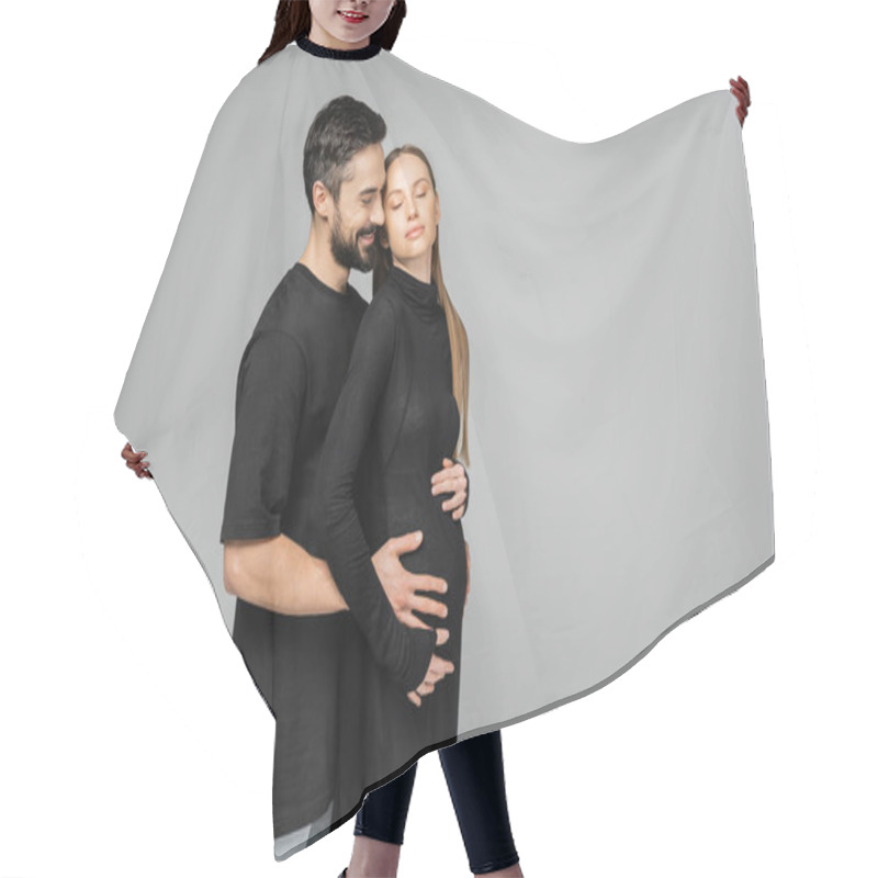 Personality  Joyful Bearded Man In T-shirt Hugging Belly Of Stylish And Relaxed Pregnant Wife In Black Dress While Standing With Closed Eyes Isolated On Grey, Growing New Life Concept Hair Cutting Cape