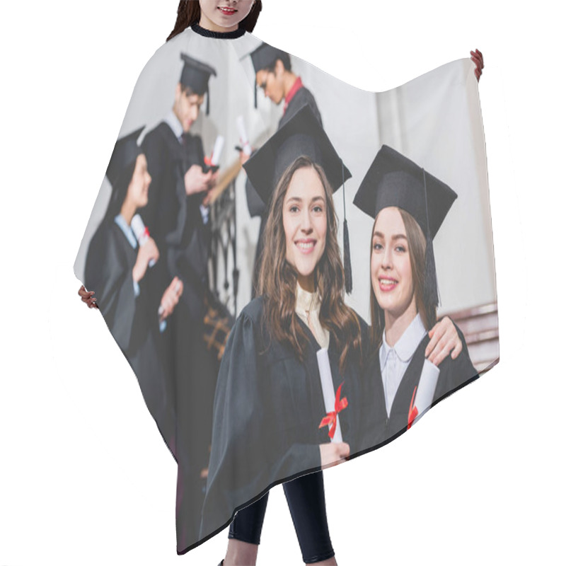 Personality  Selective Focus Of Beautiful Girls In Graduation Caps Smiling While Holding Diplomas Near Students Hair Cutting Cape