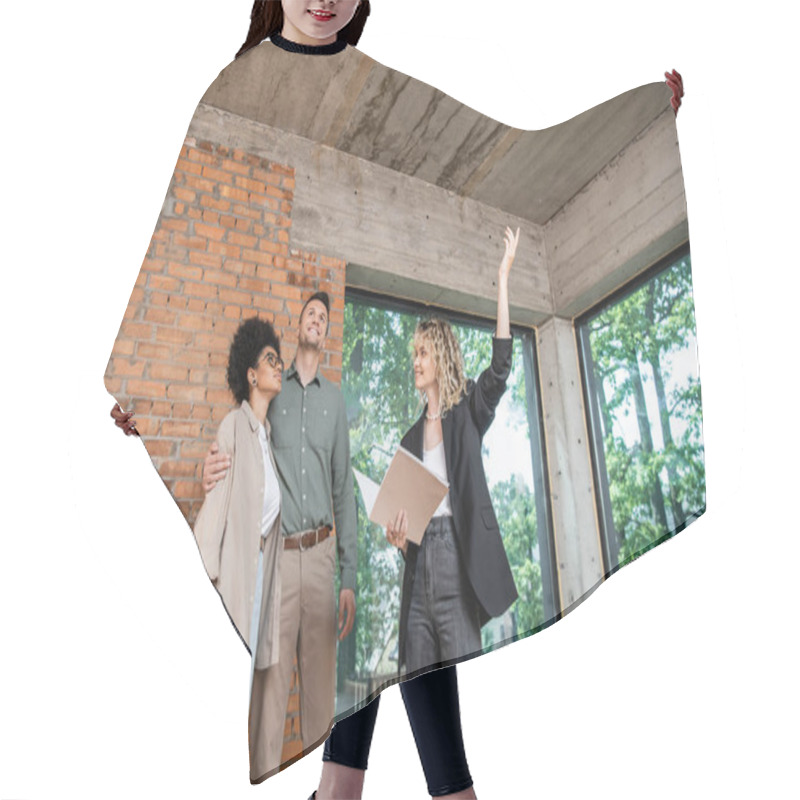 Personality  Real Estate Agent Pointing Up With Hand At Ceiling While Showing New House To Multiethnic Couple Hair Cutting Cape