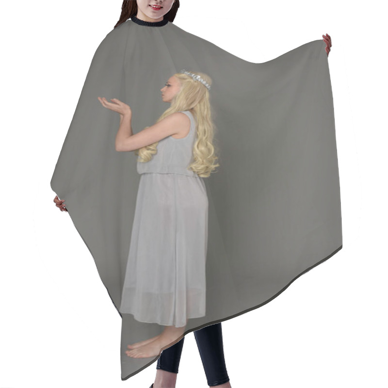 Personality  Full Length Portrait Of Blonde Girl Wearing Crow And Grey Dress, Standing Pose In Side Profile.  Grey Studio Background. Hair Cutting Cape