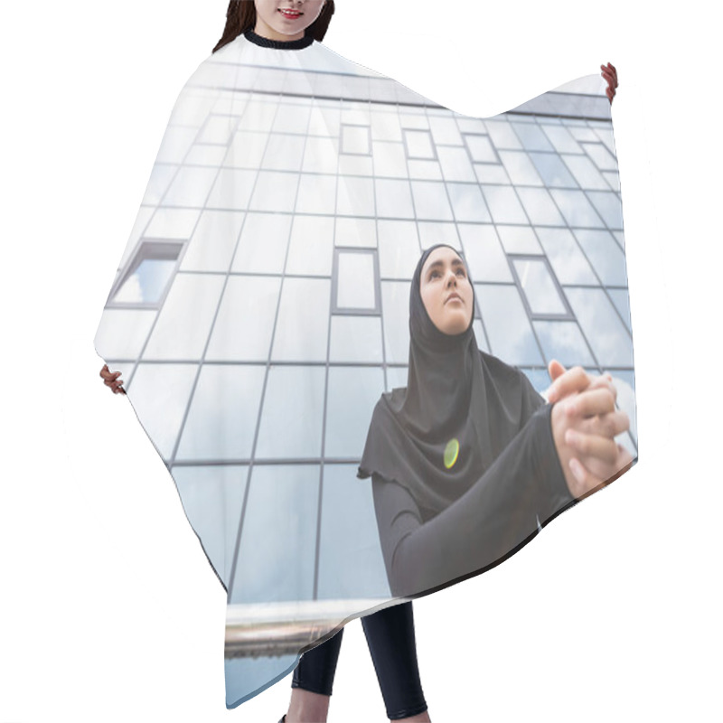 Personality  Low Angle View Of Muslim Woman In Hijab Standing With Clenched Hands Near Modern Building  Hair Cutting Cape