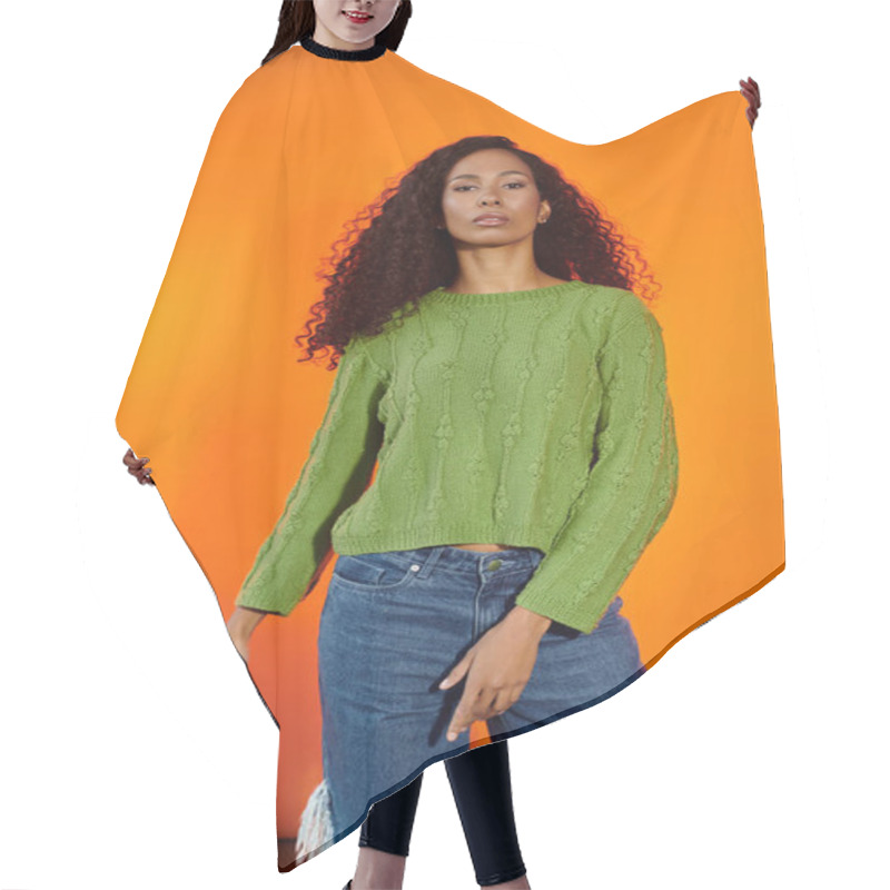 Personality  A Stylish Woman Confidently Poses In A Green Sweater Against An Orange Background. Hair Cutting Cape