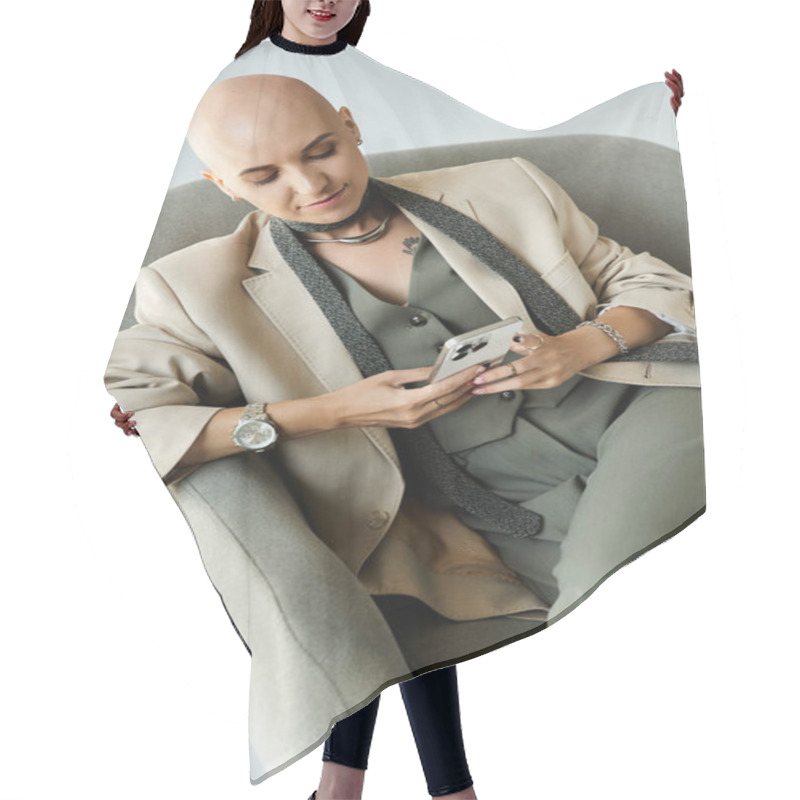 Personality  A Confident Young Woman With Alopecia Relaxes In A Stylish Chair, Engaged With Her Smartphone. Hair Cutting Cape