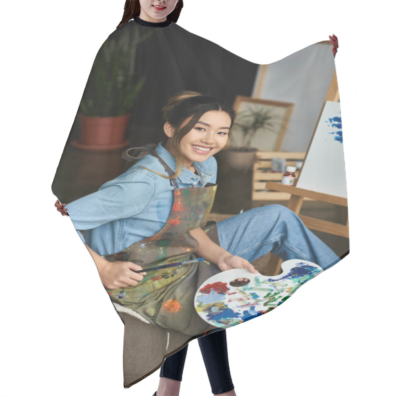 Personality  A Young Asian Artist In A Workshop, Wearing An Apron, Smiles While Holding A Paintbrush And Palette. Hair Cutting Cape