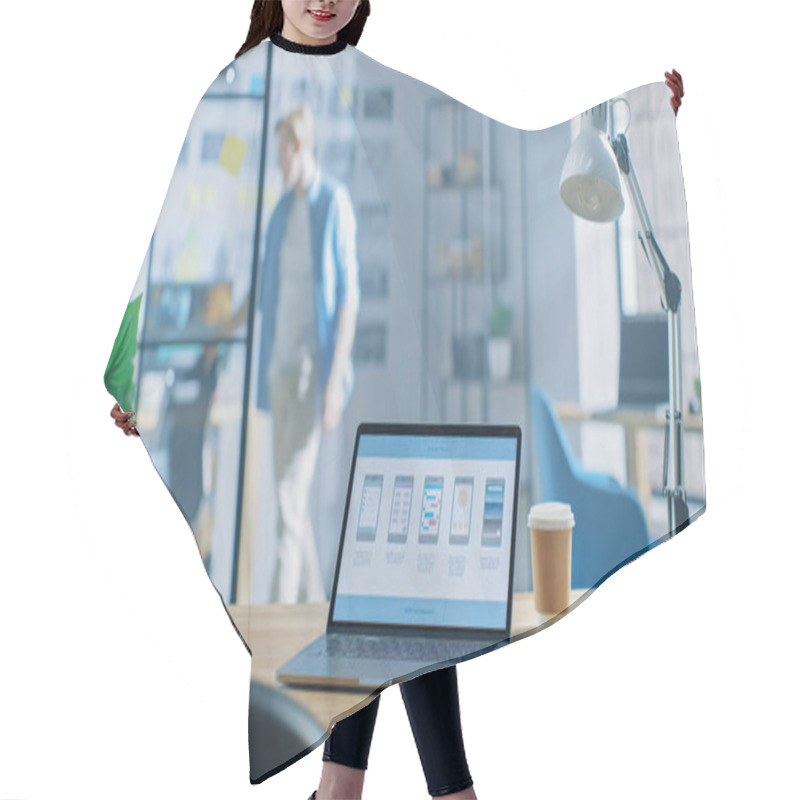 Personality  Shot Of Laptop Standing At Desk In The Creative Office. Notebook Screen Shows Mobile Phone Application Design, Software UI Development. In Background Young Professional Stans In Creative Modern Office Hair Cutting Cape