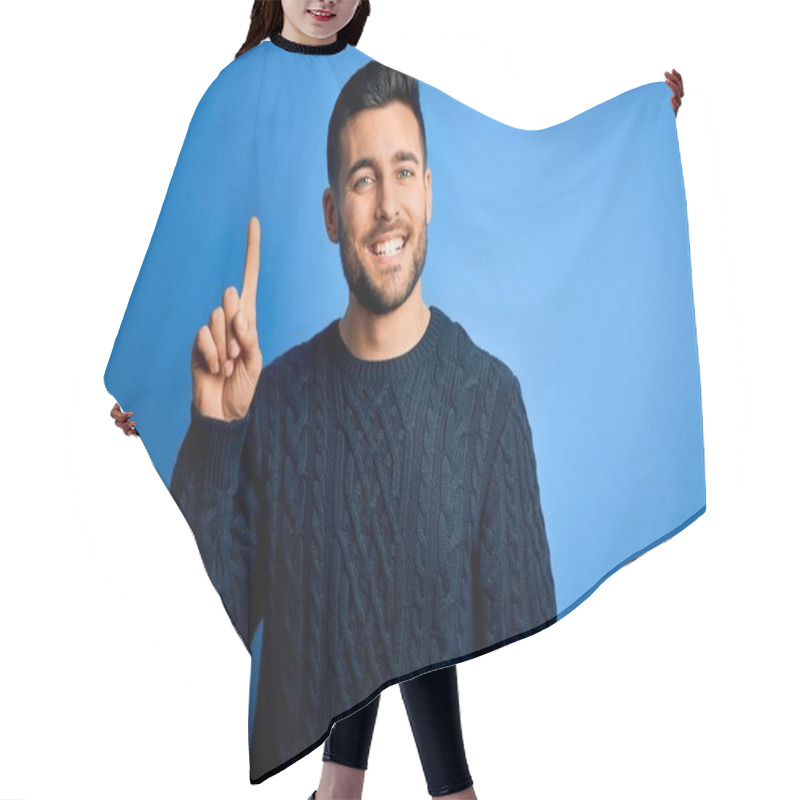 Personality  Young Handsome Man Wearing Casual Sweater Standing Over Isolated Blue Background Showing And Pointing Up With Finger Number One While Smiling Confident And Happy. Hair Cutting Cape