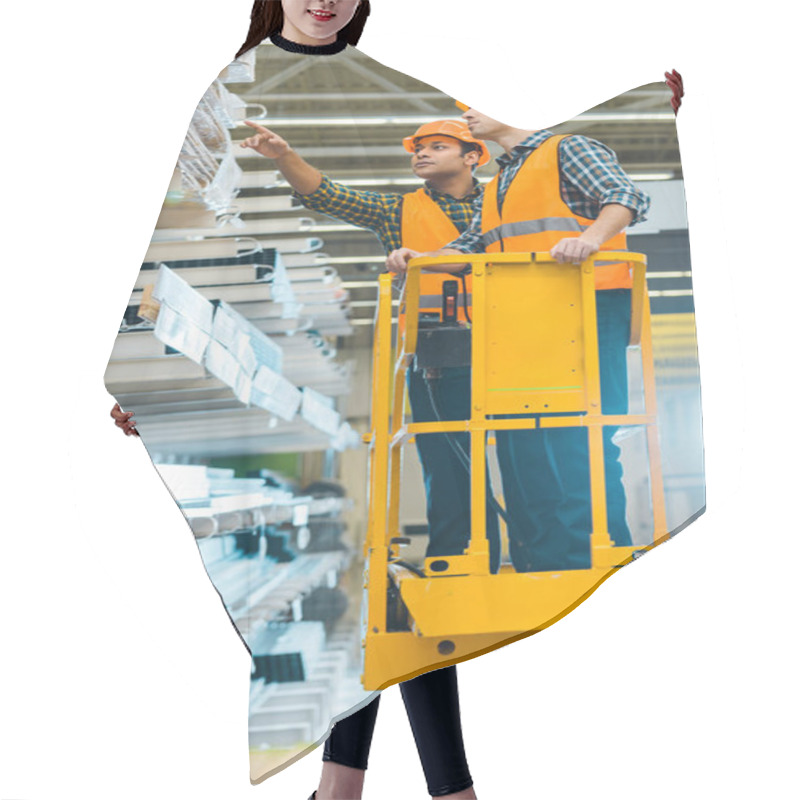 Personality  Serious Indian Worker Pointing With Finger At Construction Materials While Standing On Scissor Lift Near Colleague  Hair Cutting Cape