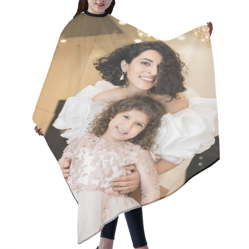 Personality  Charming Middle Eastern Bride With Brunette Hair Standing In White Wedding Gown With Puff Sleeves And Ruffles Behind Cute Daughter And Smiling Together In Bridal Store, Looking At Camera  Hair Cutting Cape