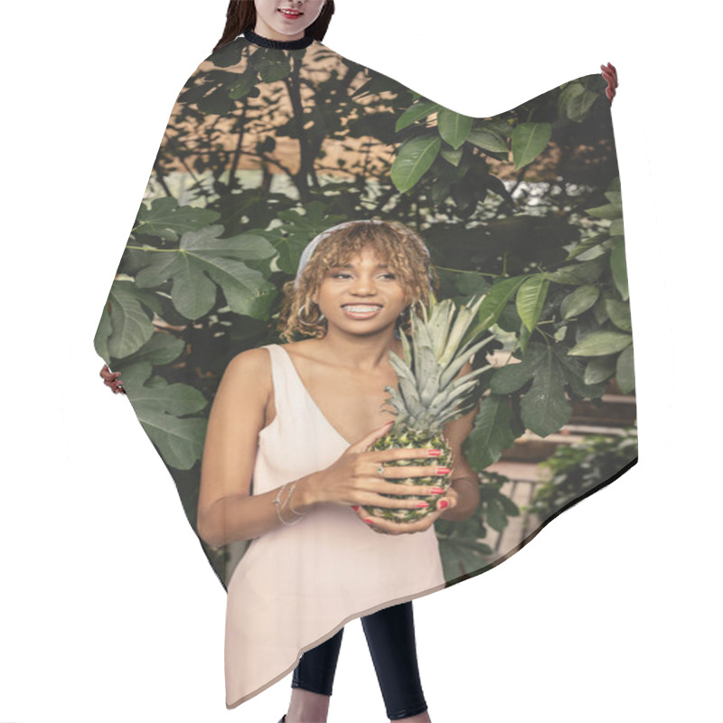 Personality  Young And Cheerful African American Woman With Braces Wearing Summer Outfit And Holding Pineapple While Standing Near Plants In Orangery, Woman In Summer Outfit Posing Near Lush Tropical Plants Hair Cutting Cape