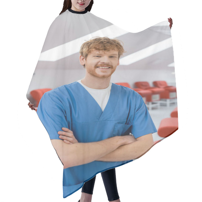 Personality  Redhead Healthcare Worker In Blue Uniform Standing With Folded Arms And Smiling At Camera Near Comfortable Medical Chairs In Blood Donation Center, Blurred Background Hair Cutting Cape