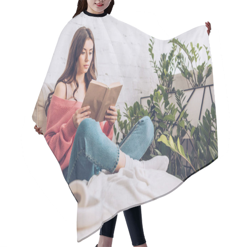 Personality  Selective Focus Of Focused Young Woman Reading Book While Sitting With Crossed Legs Near Green Plants At Home Hair Cutting Cape